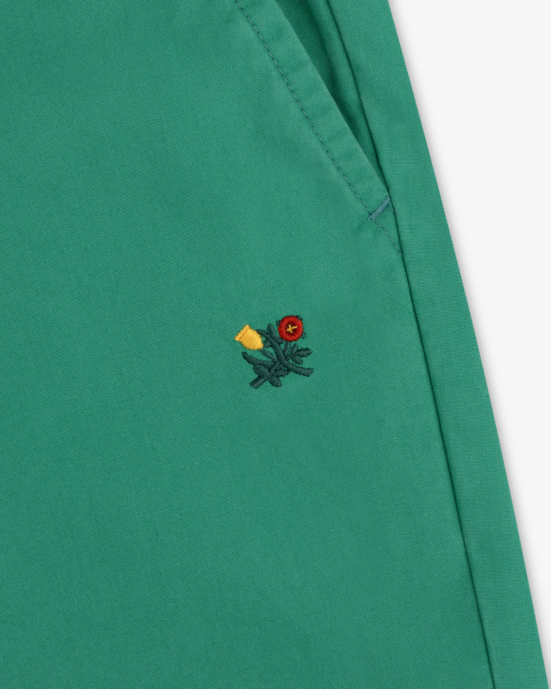 Washed Cotton Windbreaker Pant in green with pocket and small embroidered flower—red center, yellow petals, green stem.