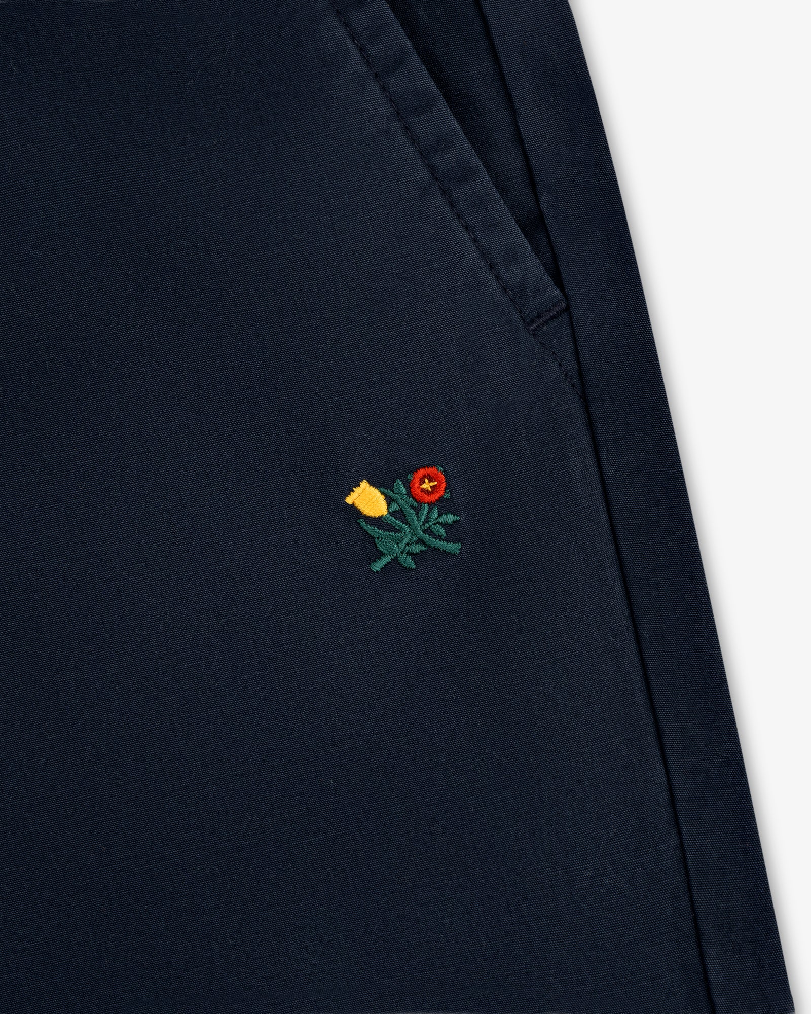 Close-up of the Washed Cotton Windbreaker Pant in navy blue with a small yellow and red flower near the pocket.