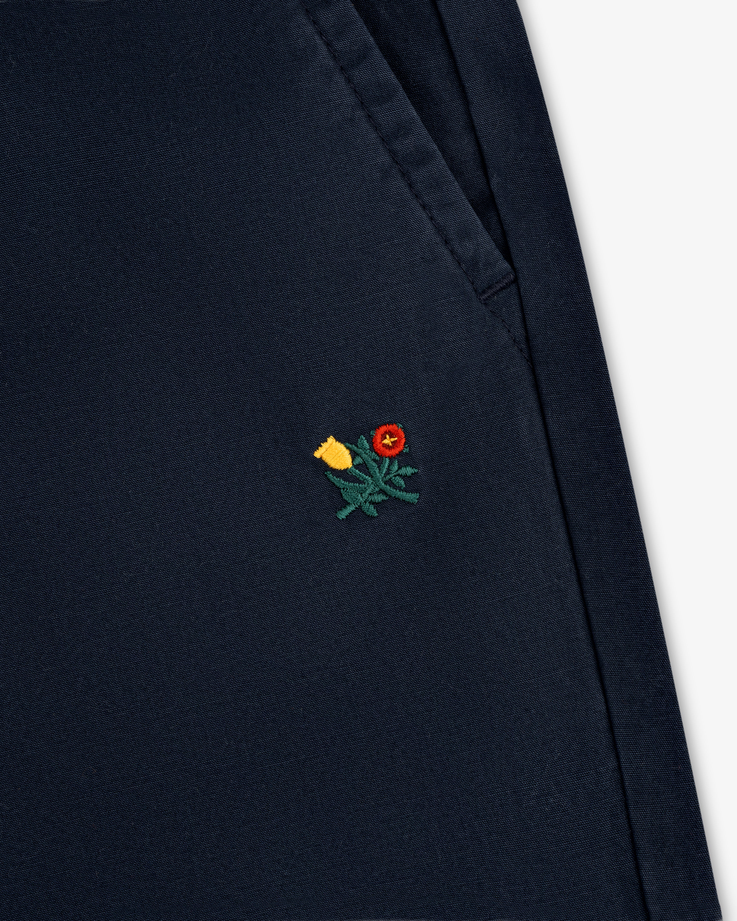 Close-up of the Washed Cotton Windbreaker Pant in navy blue with a small yellow and red flower near the pocket.