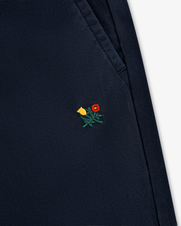 Close-up of the Washed Cotton Windbreaker Pant in navy blue with a small yellow and red flower near the pocket.