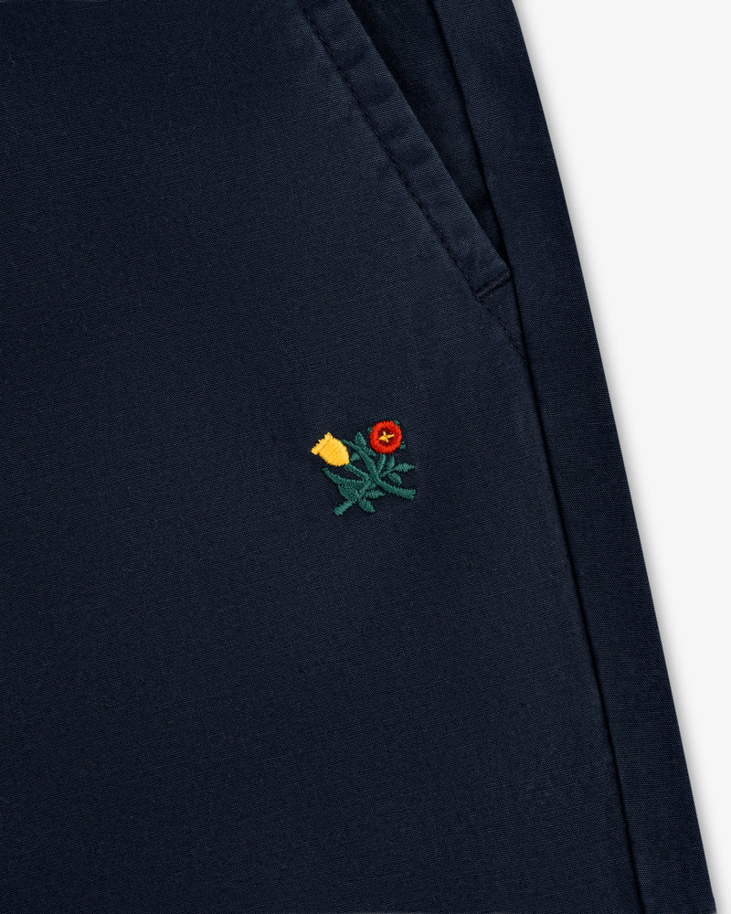 Close-up of the Washed Cotton Windbreaker Pant in navy blue with a small yellow and red flower near the pocket.