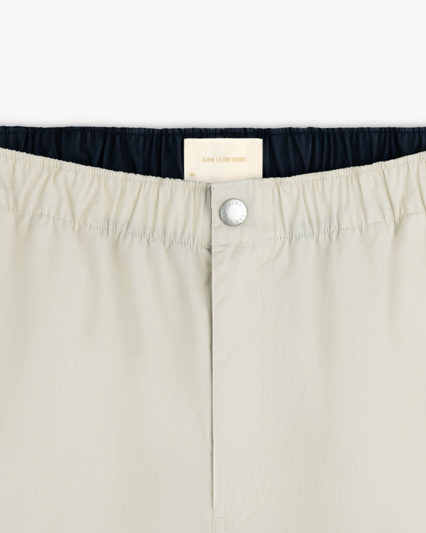 Close-up of Washed Cotton Windbreaker Pant in beige with elastic waistband, button closure, and Aimé Leon Dore label.