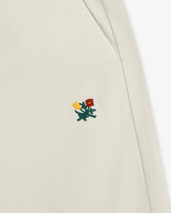 Close-up of a Washed Cotton Windbreaker Pant in cream with a small red and yellow embroidered flower near the seam.