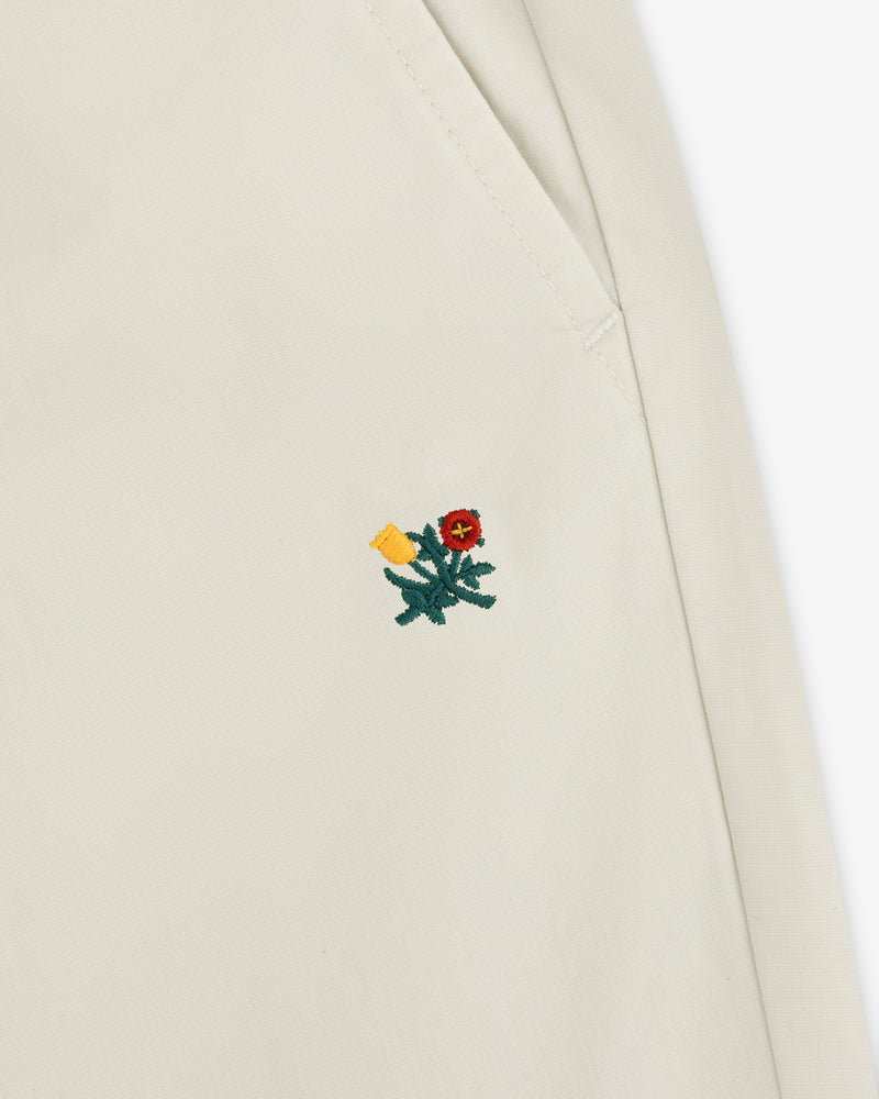 Close-up of a Washed Cotton Windbreaker Pant in cream with a small red and yellow embroidered flower near the seam.