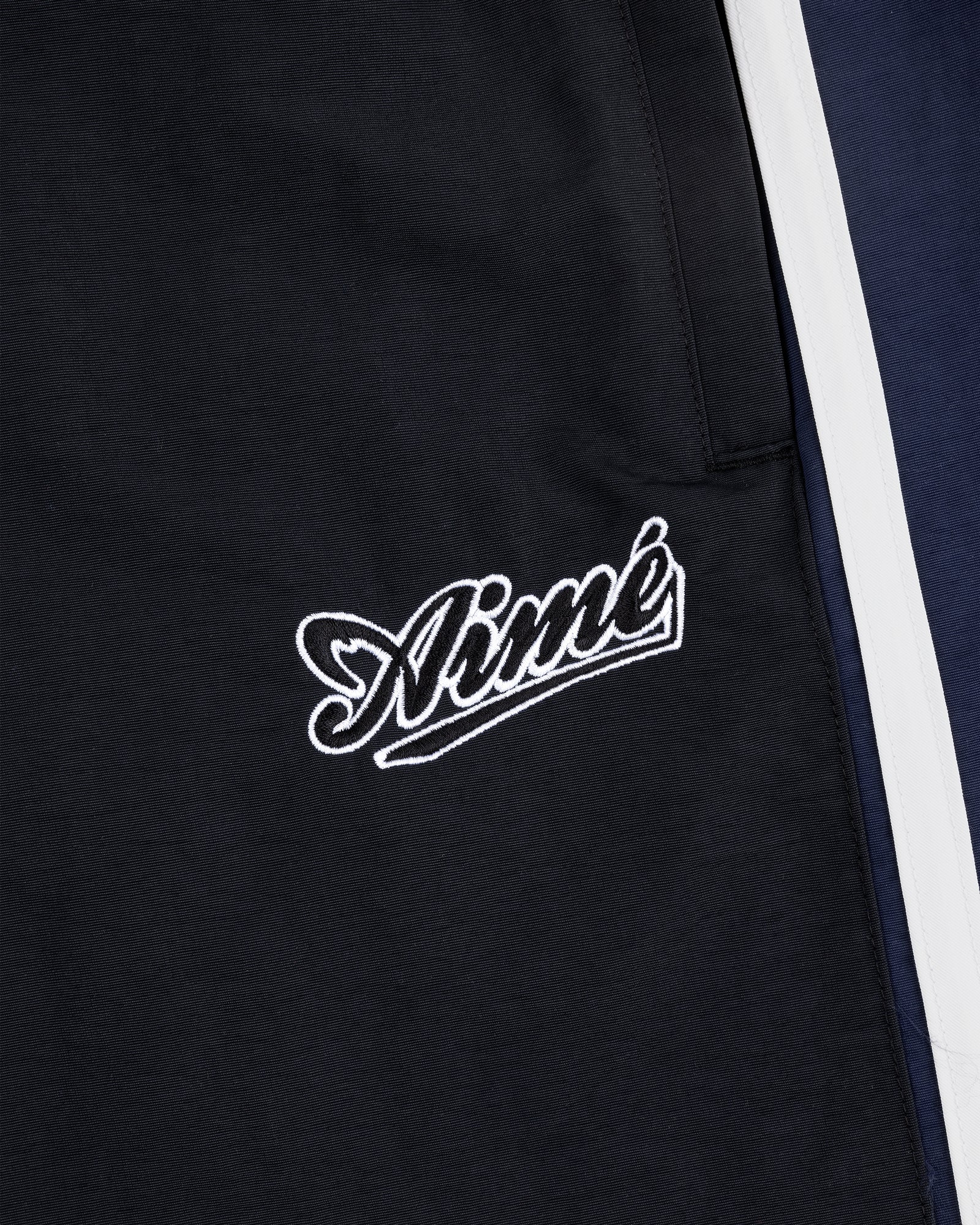 Close-up of black Colorblock Track Pant with Aimé embroidered in white cursive near navy and white panels.