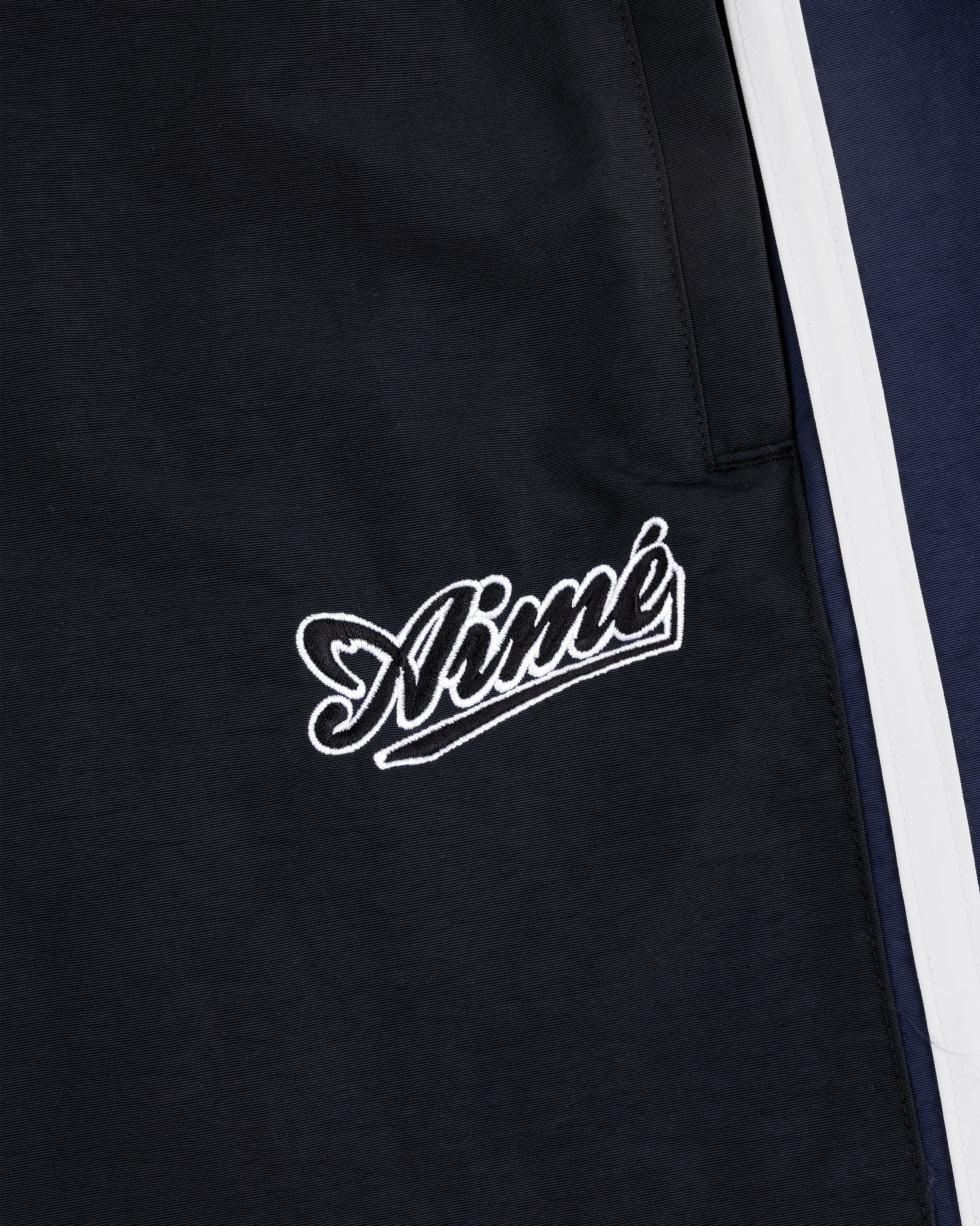 Close-up of black Colorblock Track Pant with Aimé embroidered in white cursive near navy and white panels.
