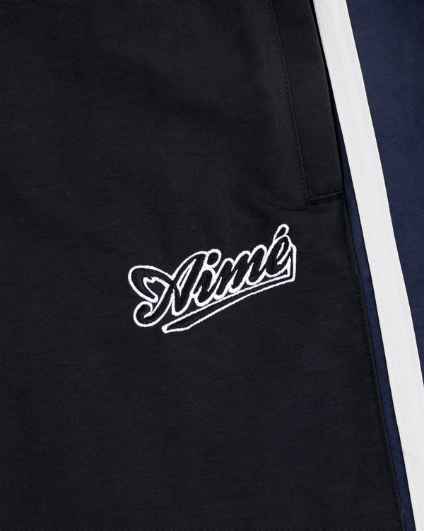 Close-up of black Colorblock Track Pant with Aimé embroidered in white cursive near navy and white panels.