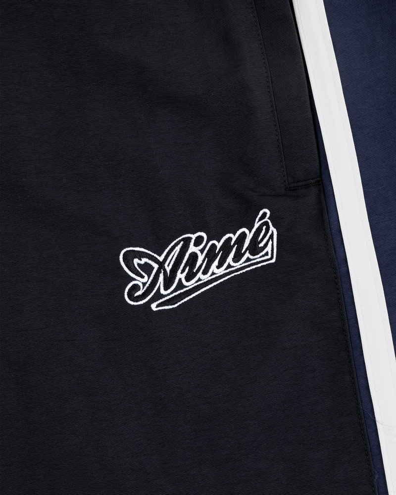 Close-up of black Colorblock Track Pant with Aimé embroidered in white cursive near navy and white panels.