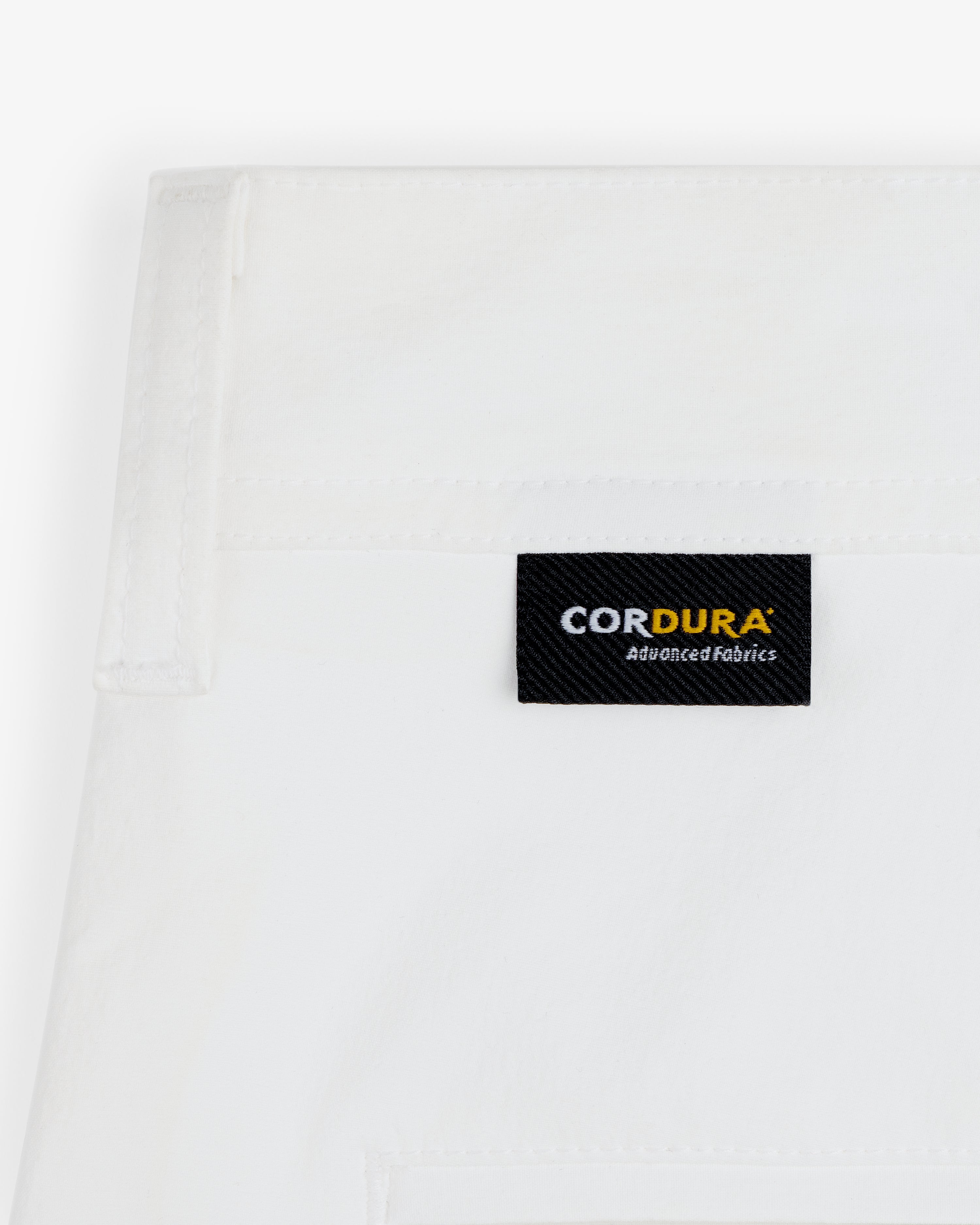 Close-up of ALD Golf Cordura Double Pleated Pant's white fabric with a black CORDURA Advanced Fabrics label stitched on.