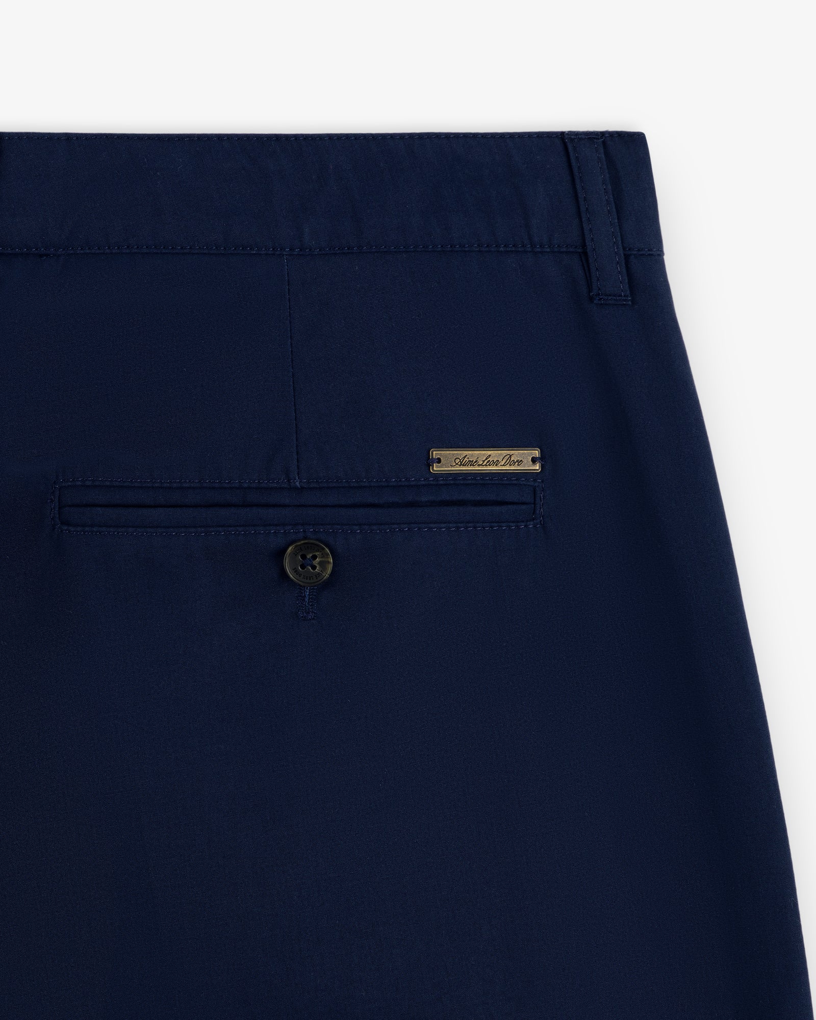 Close-up of the back pocket with button and metal label on Lightweighted Pleated Cotton Trouser in navy blue.