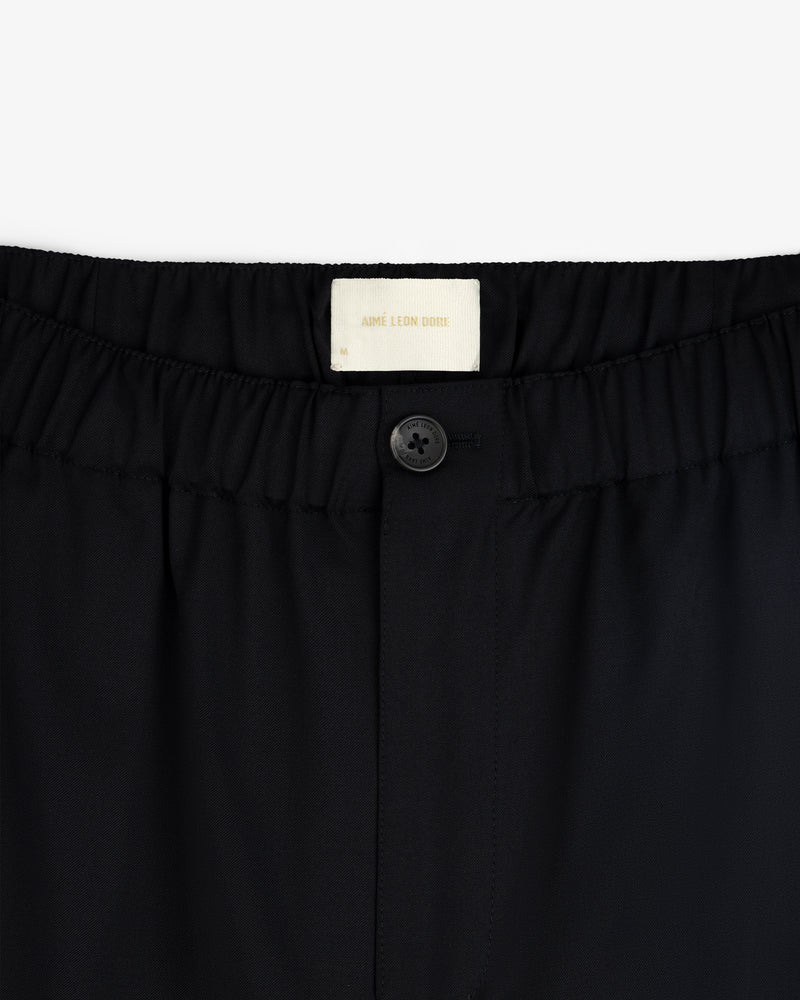 Close-up of Elasticated Waist Gabardine Trouser in black with a button closure and visible Aimé Leon Dore label.