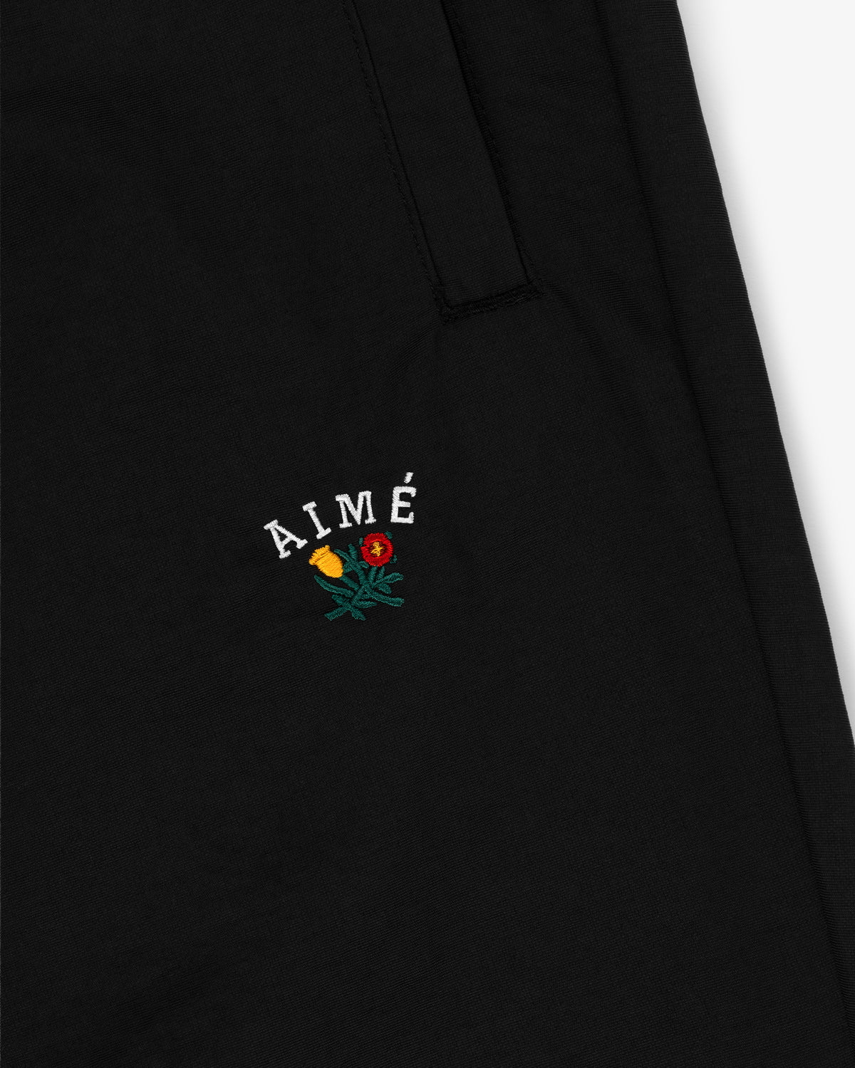 Close-up of black Crest Nylon Track Pant with AIMÉ text and embroidered yellow and red rose below it.