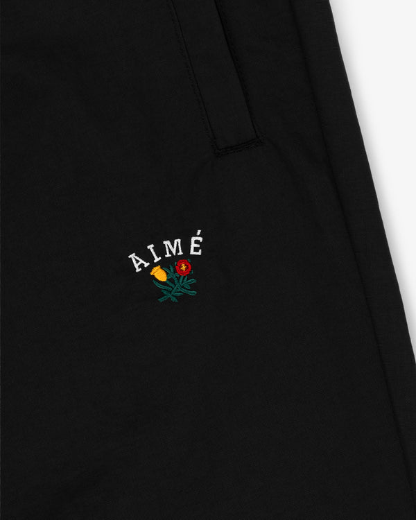 Close-up of black Crest Nylon Track Pant with AIMÉ text and embroidered yellow and red rose below it.