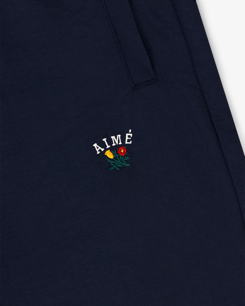 Navy blue Crest Nylon Track Pant with AIMÉ text and a small embroidered yellow-red flower below the pocket.