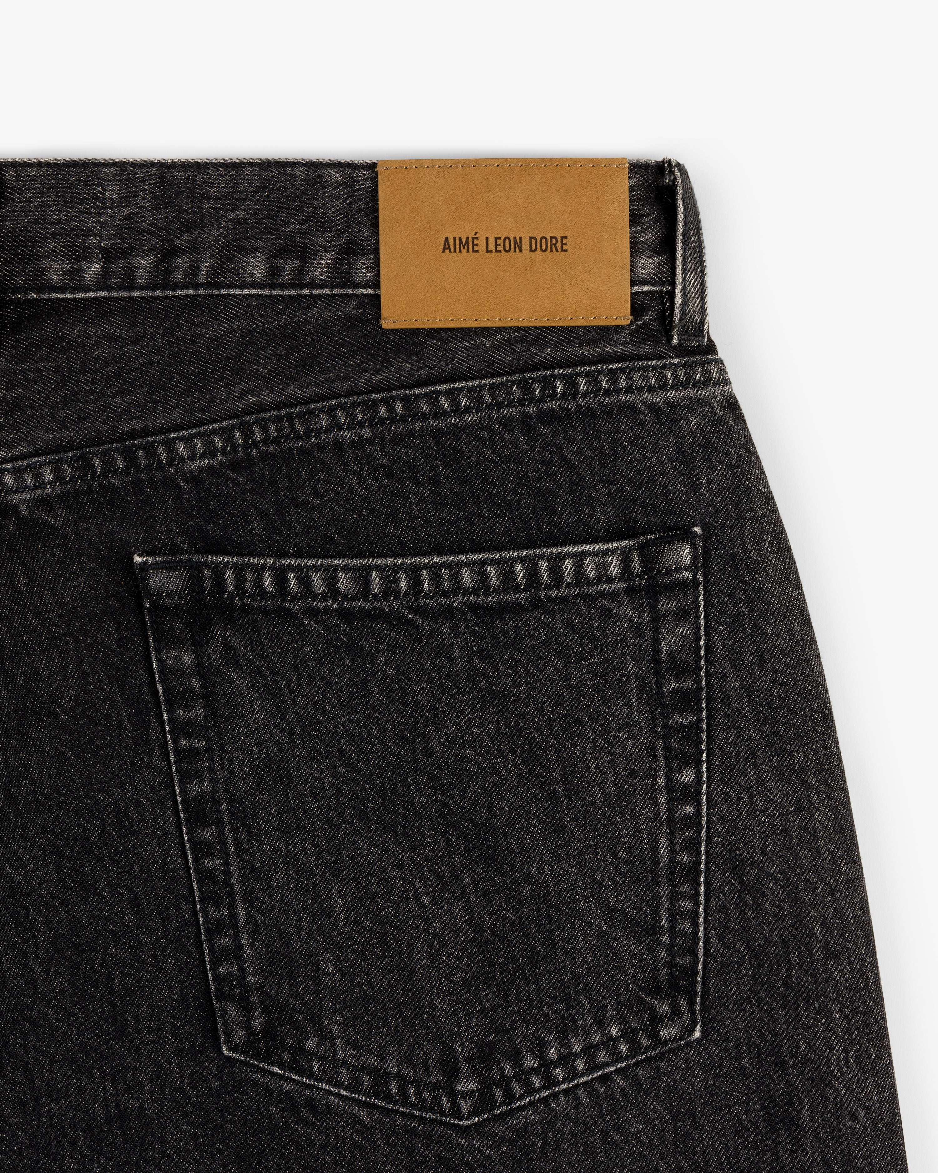 Back pocket of Relaxed Fit 5-Pocket Denim Pant with brown Aimé Leon Dore label on white background.