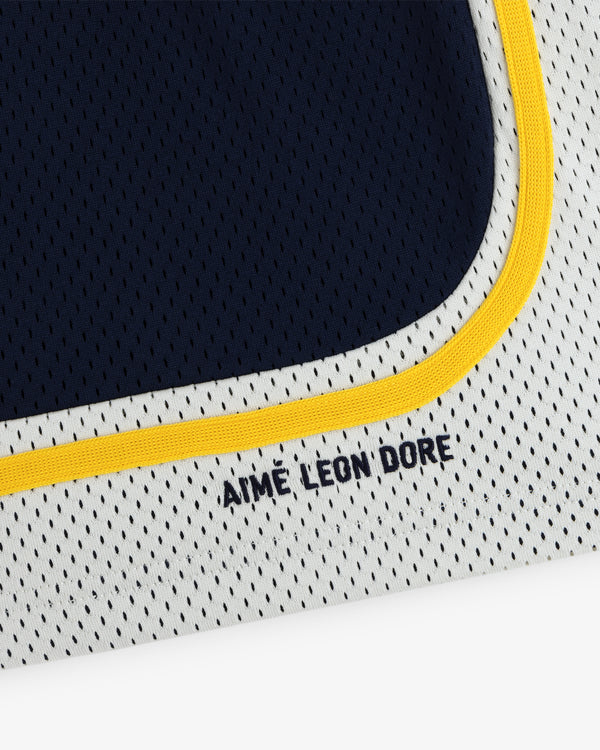 Close-up of Colorblock Court Short mesh fabric with AIME LEON DORE text and yellow trim on blue and white.