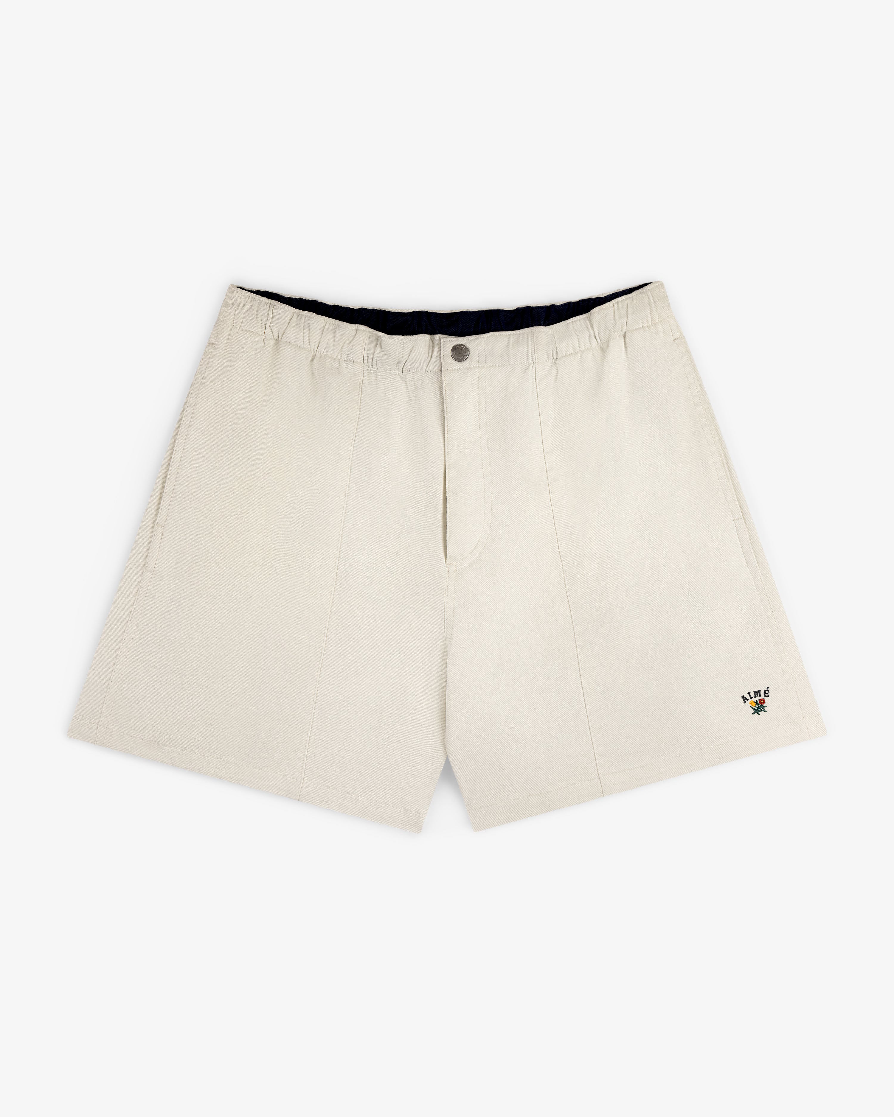 Crest Casual Short in beige with side pockets and a small floral embroidery near the hem, shown on white background.