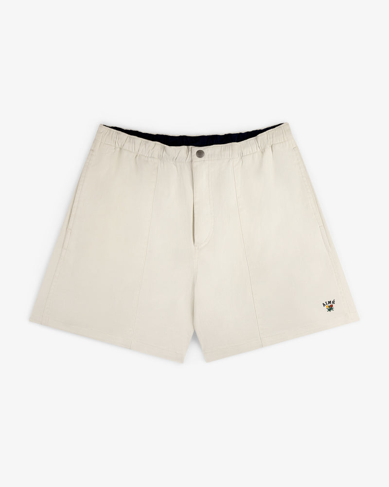 Crest Casual Short in beige with side pockets and a small floral embroidery near the hem, shown on white background.