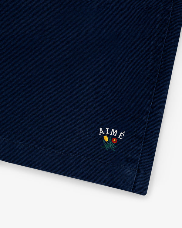 Close-up of Crest Casual Short in navy with AIMÉ and three small embroidered flowers near the hem.