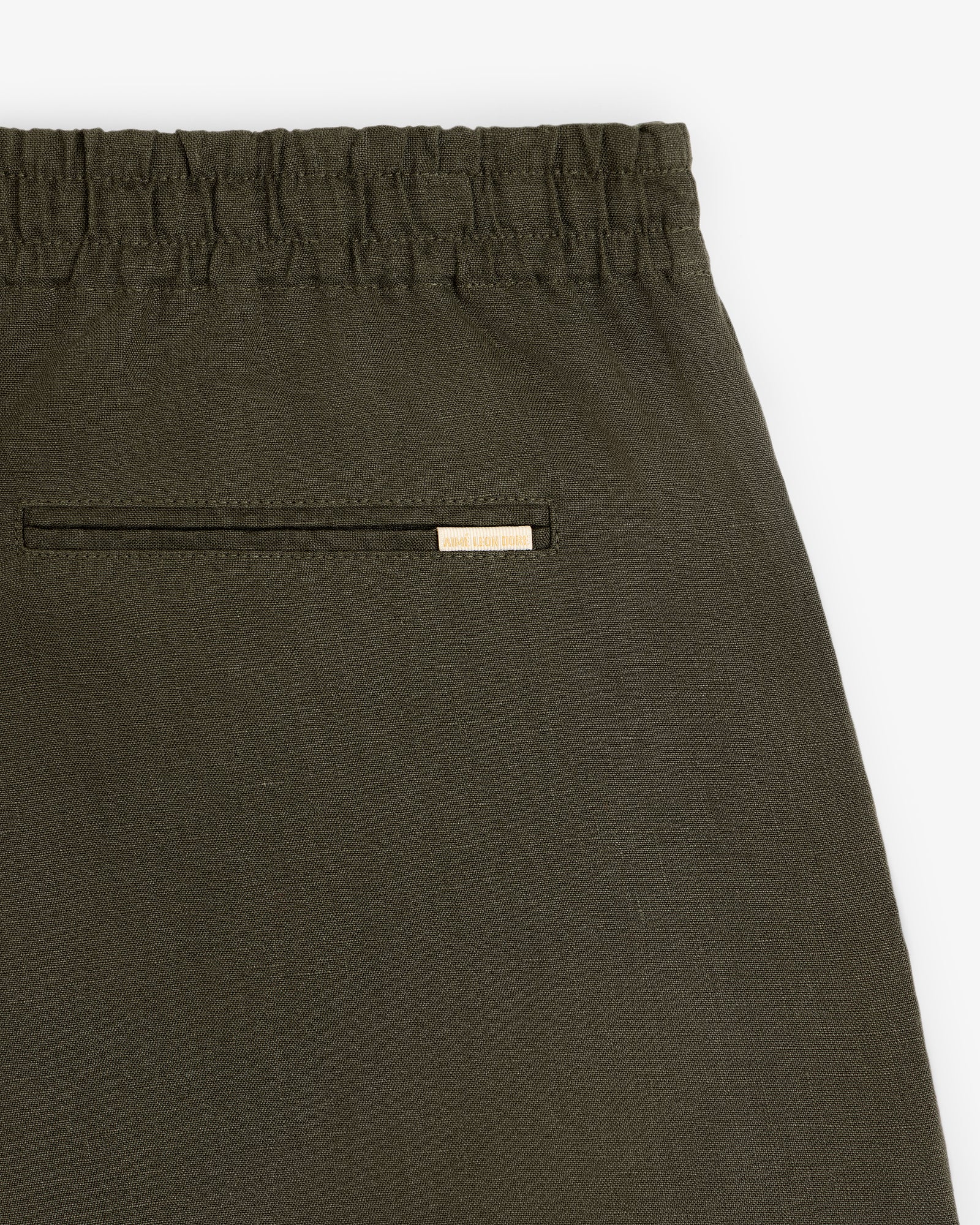 Close-up of Linen Leisure Short in olive green with elastic waistband and back pocket featuring a metallic brand tag.