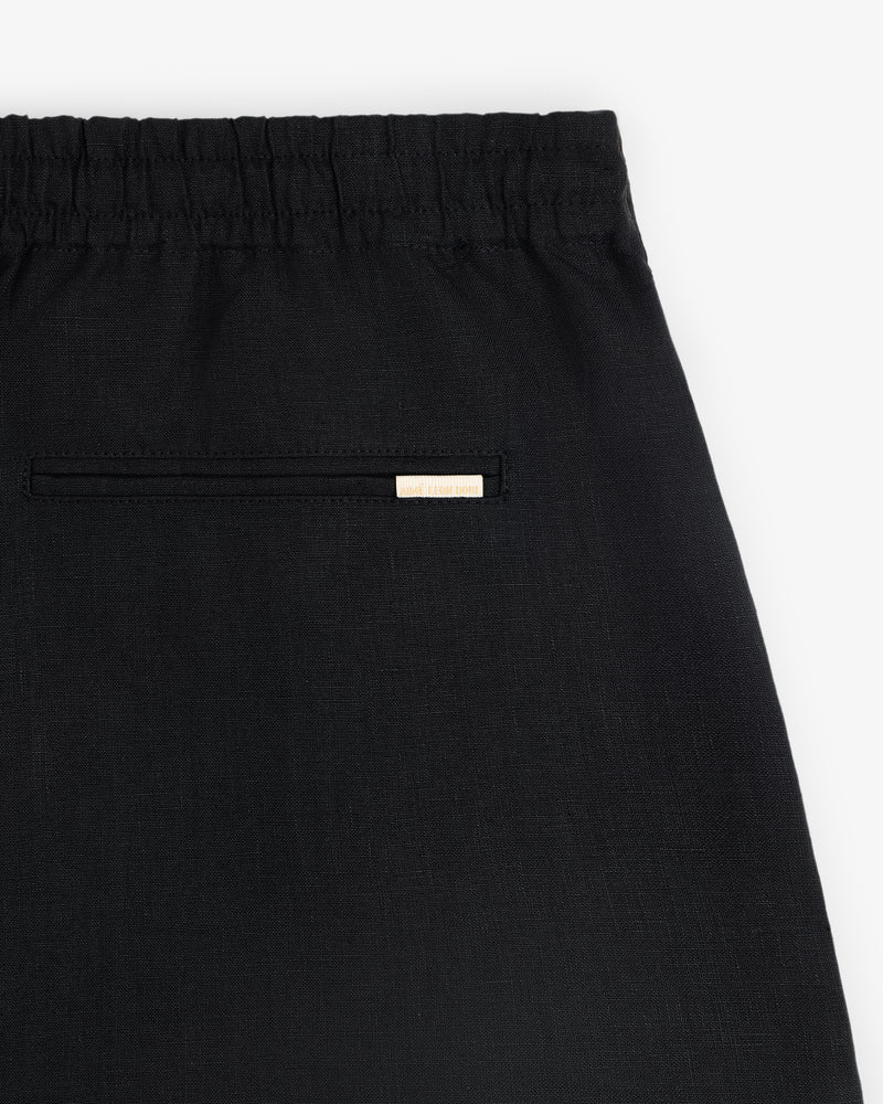 Close-up of the Linen Leisure Short in black, featuring an elastic waistband and a small back pocket with a label above.