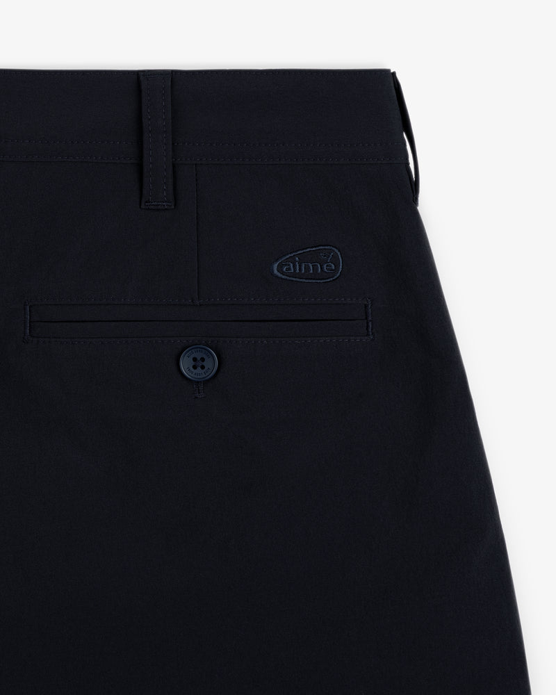 Close-up of ALD Golf Cordura Double Pleated Short's navy pocket with button and small aime logo on white background.