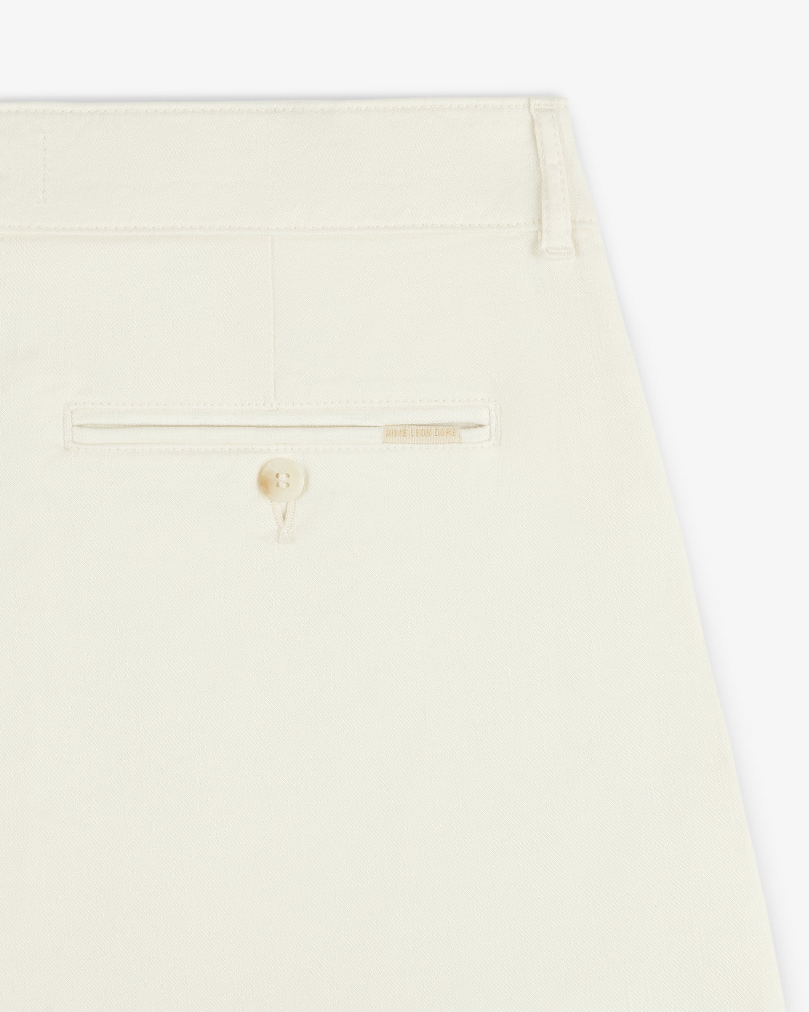 Close-up of the back pocket of Pleated Linen Blend Bermuda Short in cream with a button and beige label above the pocket.