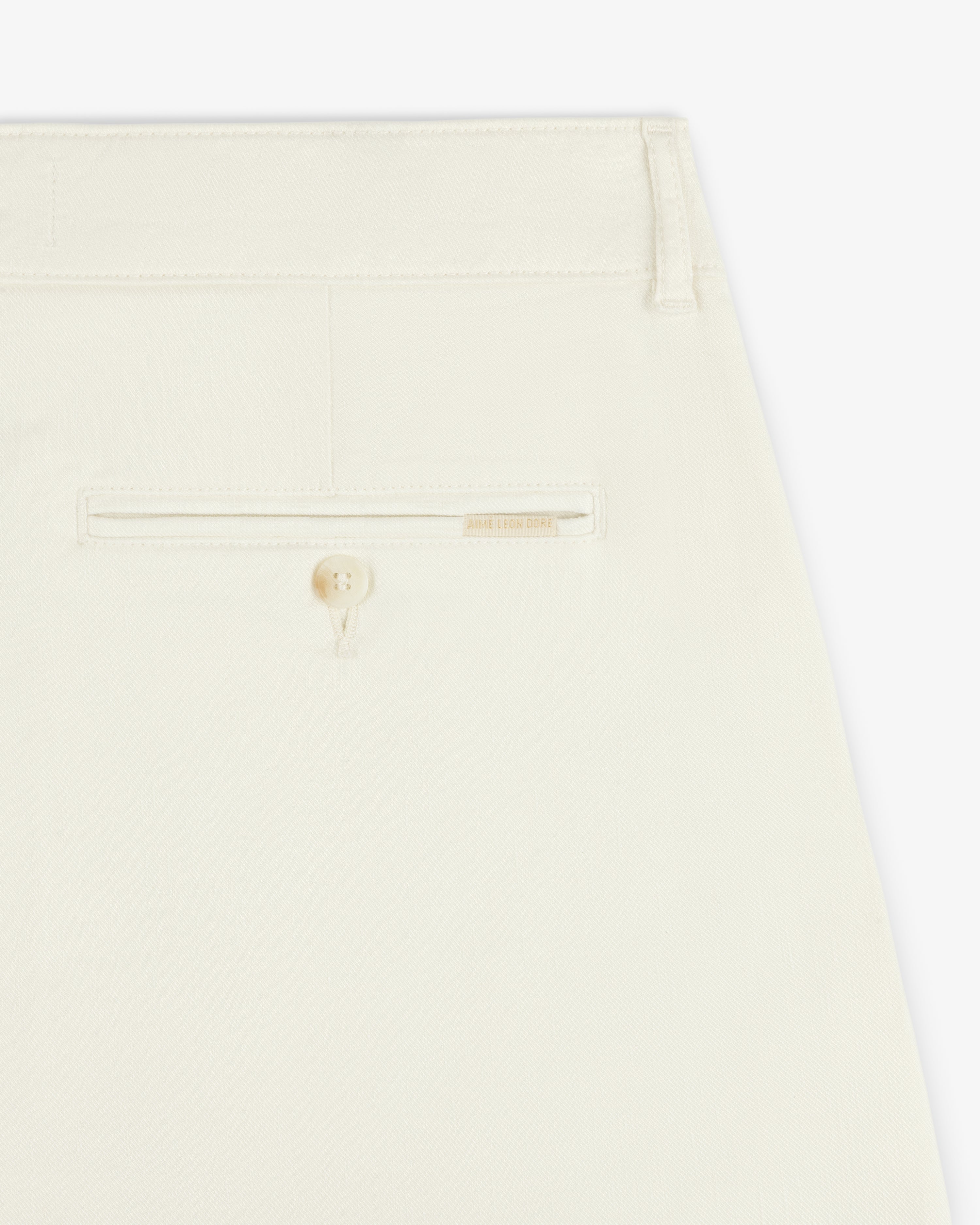 Close-up of the back pocket of Pleated Linen Blend Bermuda Short in cream with a button and beige label above the pocket.