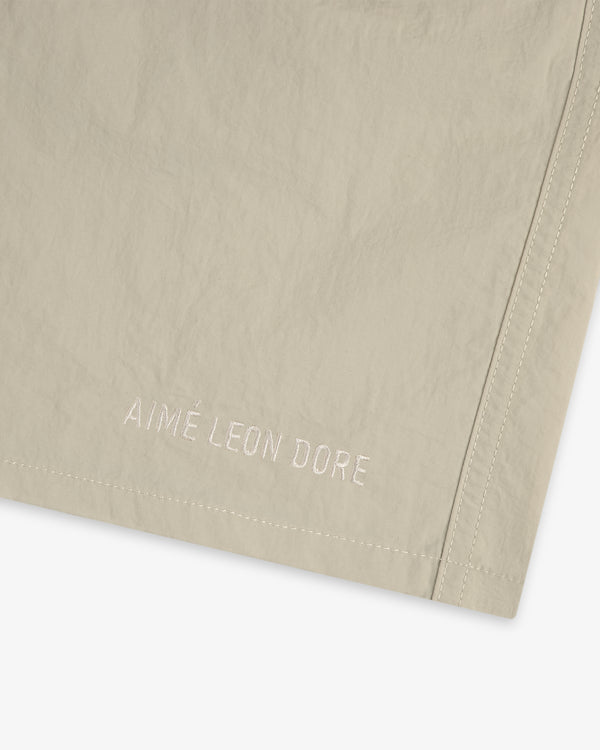 Close-up of beige Core Nylon Short with AIMÉ LEON DORE embroidered in white near a stitched edge.