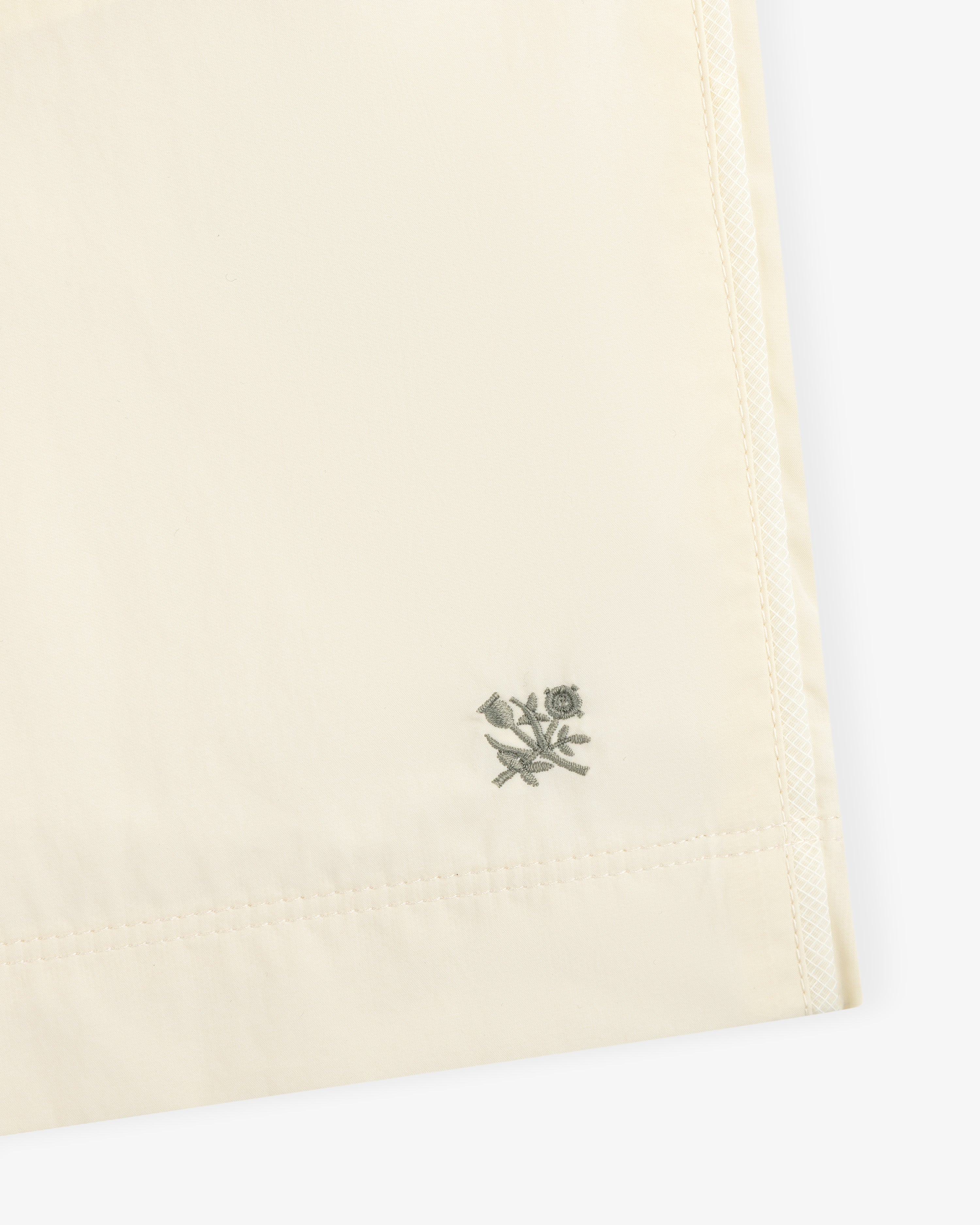 Close-up of Long Nylon Track Short in cream with a small gray embroidered flower and leaf at the corner.