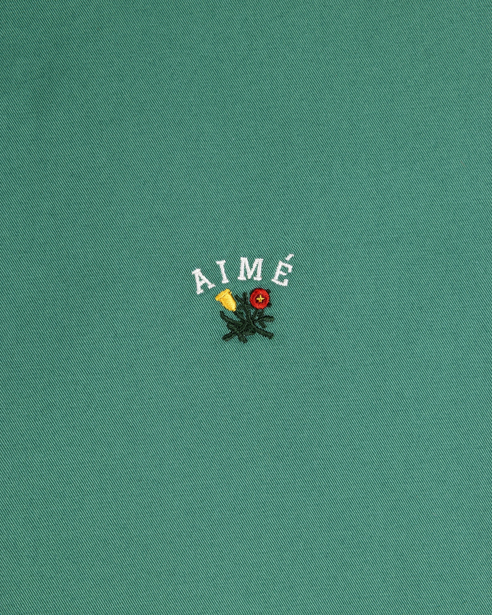 The Leon Overshirt features green fabric with AIMÉ embroidered above yellow and red flowers with green leaves.