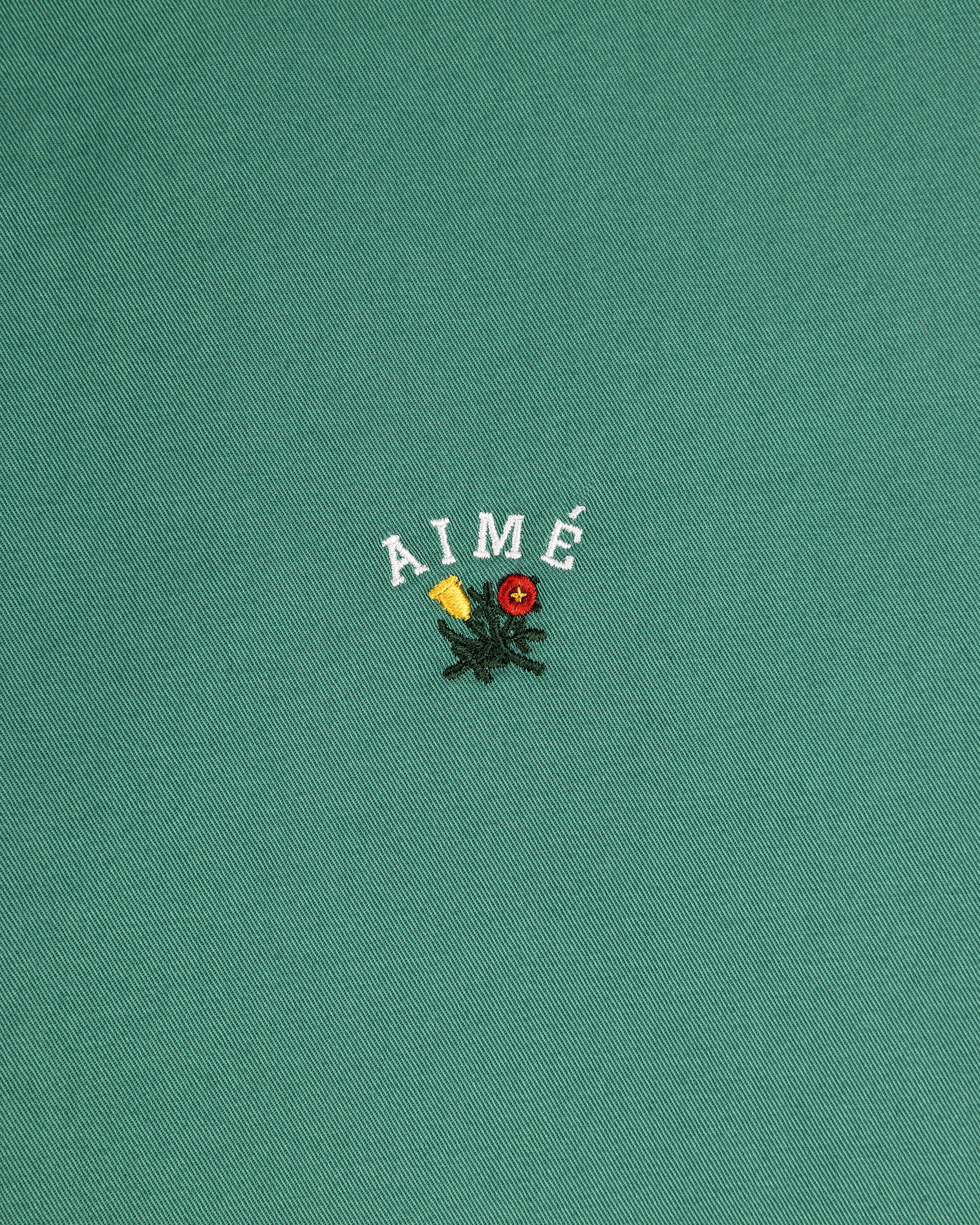 The Leon Overshirt features green fabric with AIMÉ embroidered above yellow and red flowers with green leaves.