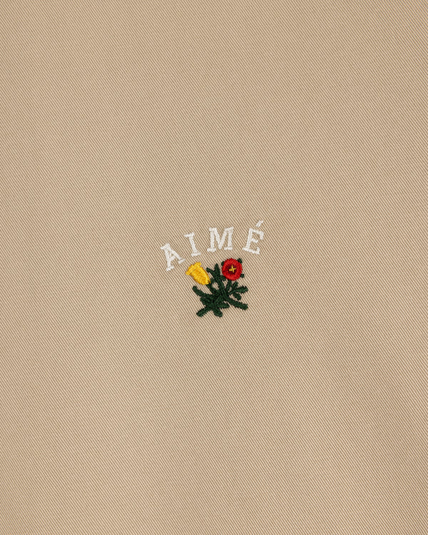 Beige Leon Overshirt with AIMÉ embroidered above a yellow and red flower with green leaves.
