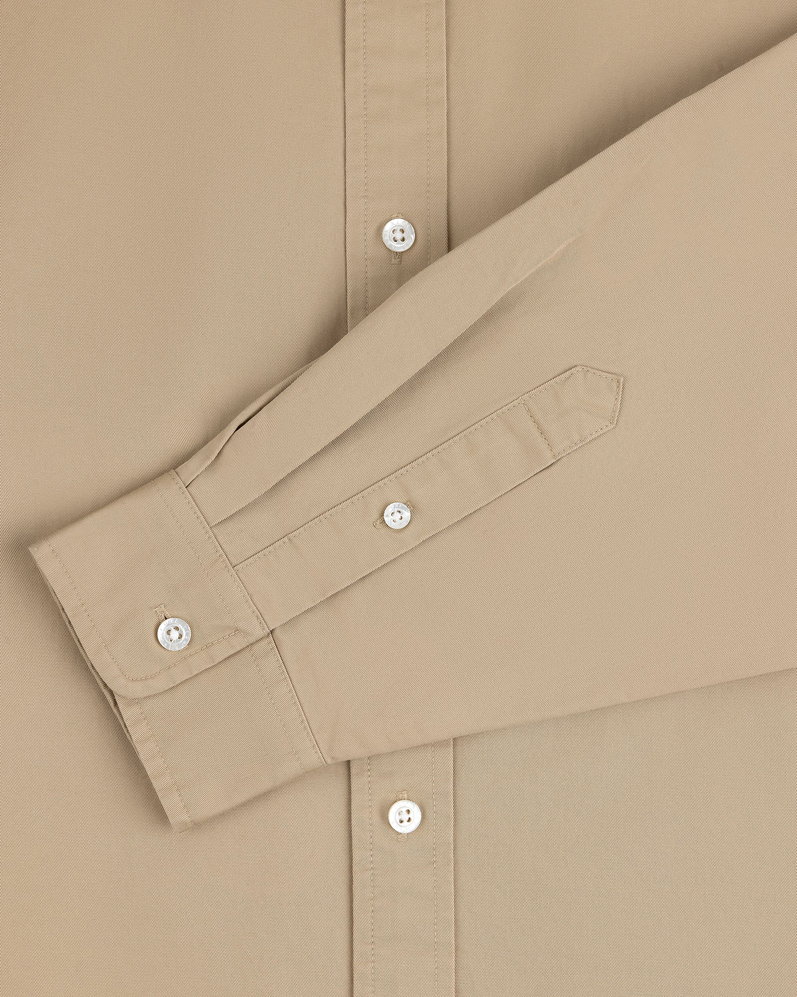 The Leon Overshirt in beige features white buttons and a long sleeve folded neatly across the front.
