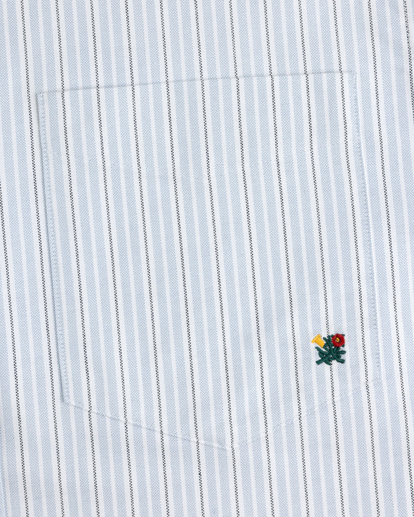 The Yarn Dyed Striped Crest Shirt is white with thin blue stripes and a small embroidered flower near the hem.