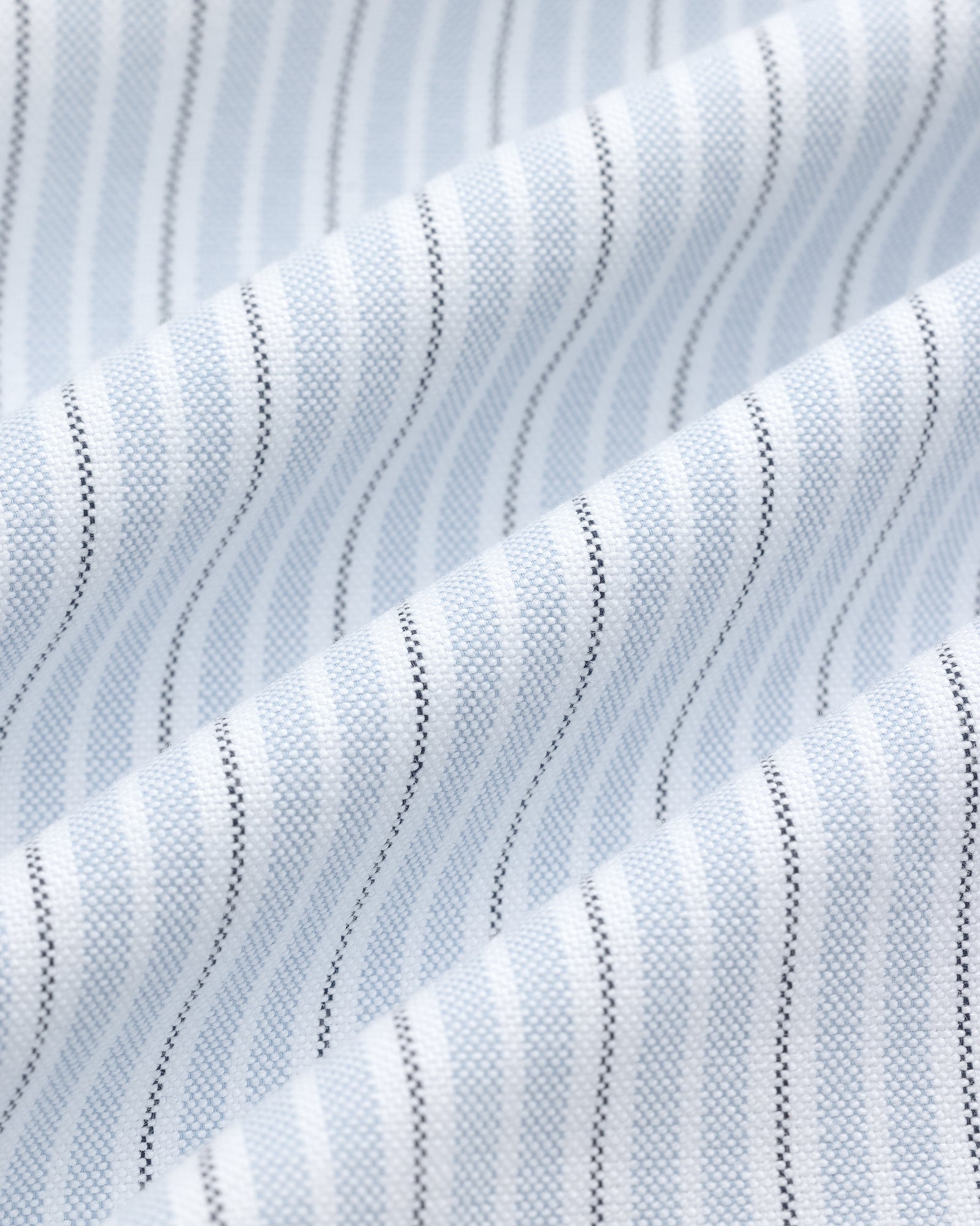 Close-up of the Yarn Dyed Striped Crest Shirt’s white fabric with light blue and black vertical pinstripes.