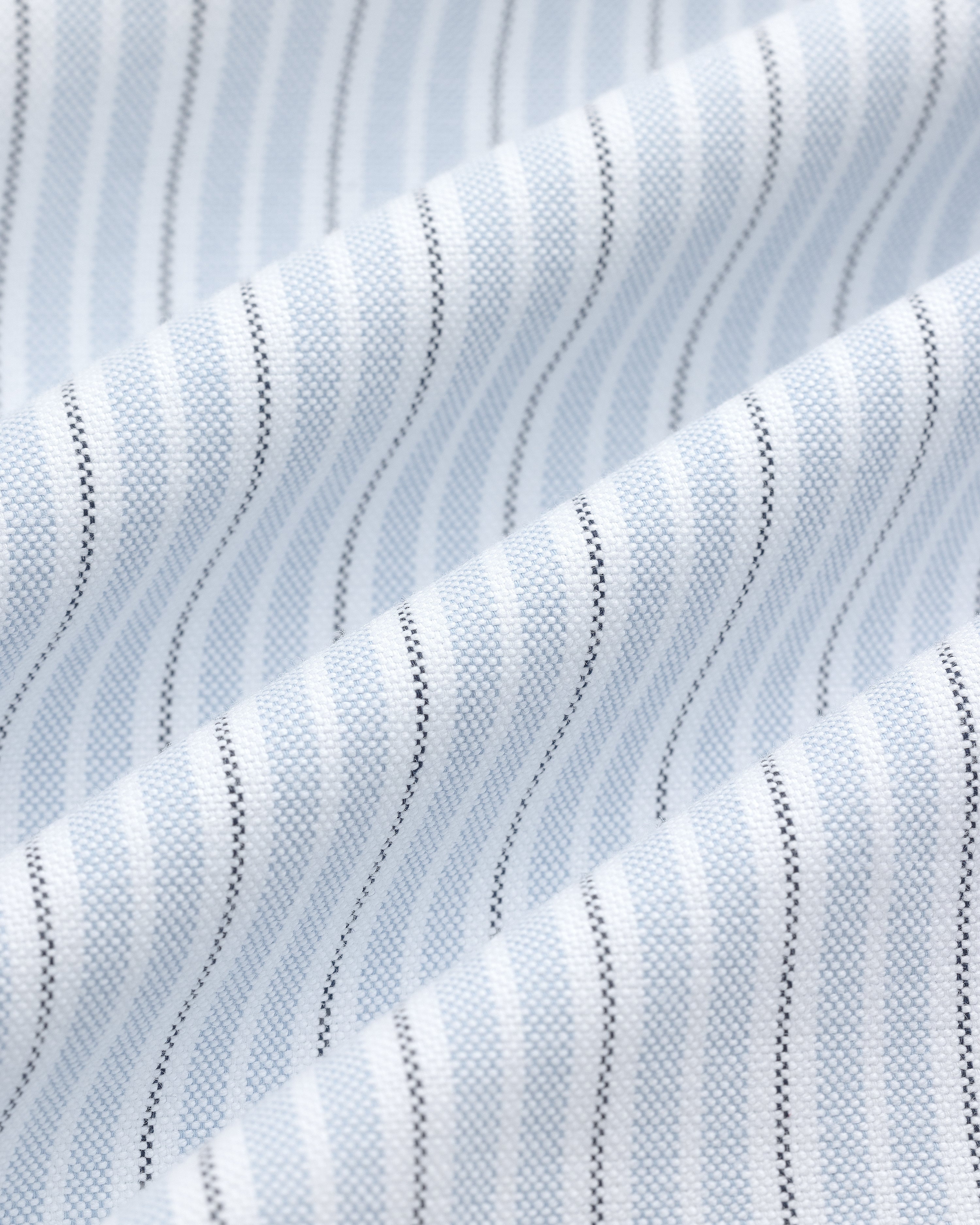 Close-up of the Yarn Dyed Striped Crest Shirt’s white fabric with light blue and black vertical pinstripes.