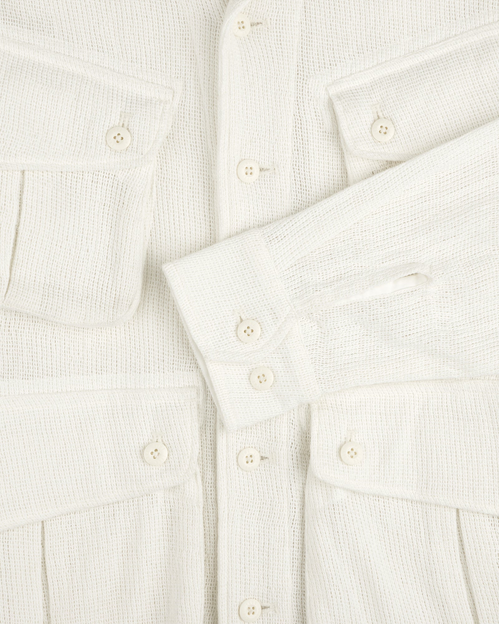 Close-up of the Mesh Jungle Shirt, cream-colored with textured fabric, buttons, flap pockets, and one sleeve across the front.
