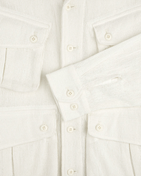 Close-up of the Mesh Jungle Shirt, cream-colored with textured fabric, buttons, flap pockets, and one sleeve across the front.