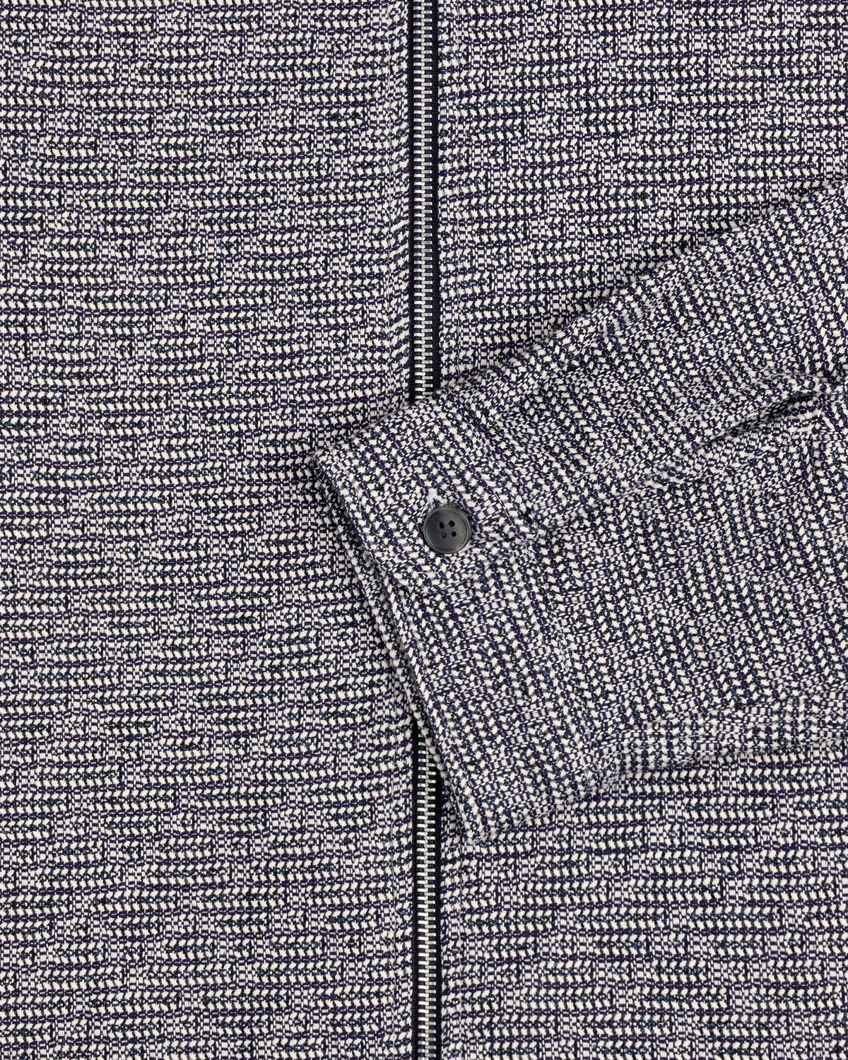 Close-up of the Textured Zip Shirt: gray and black patterned fabric with a sleeve and black button.