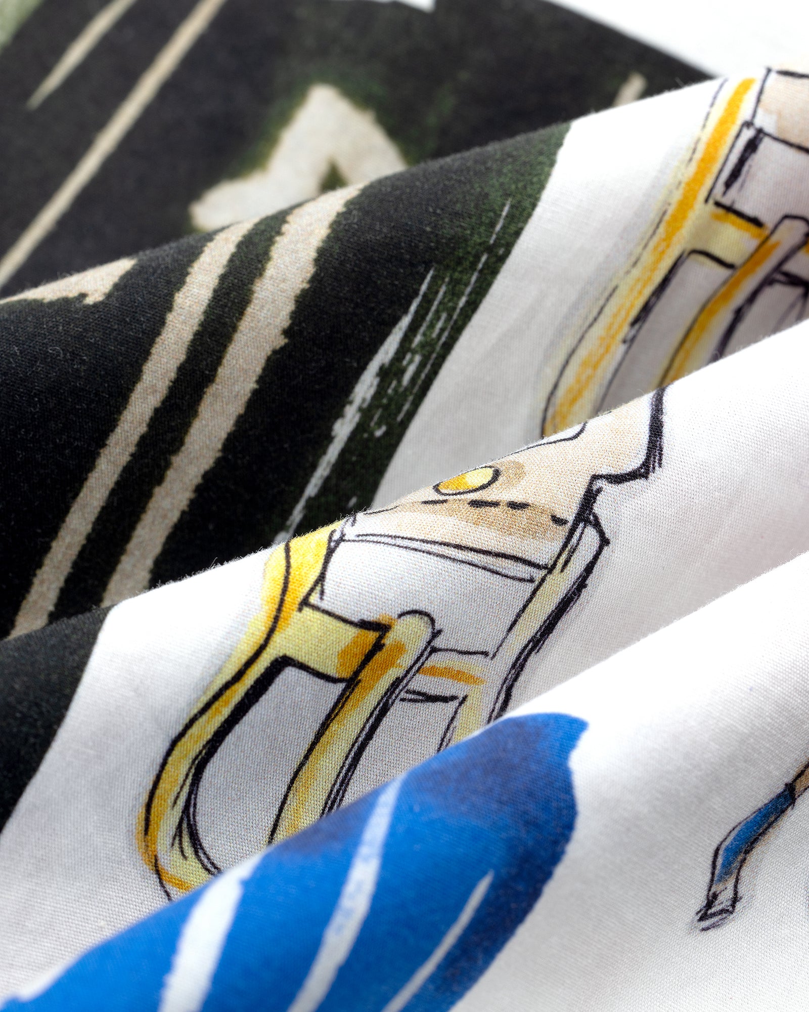Close-up of the Printed Leon Overshirt featuring abstract black, green, yellow, and blue designs on white fabric.