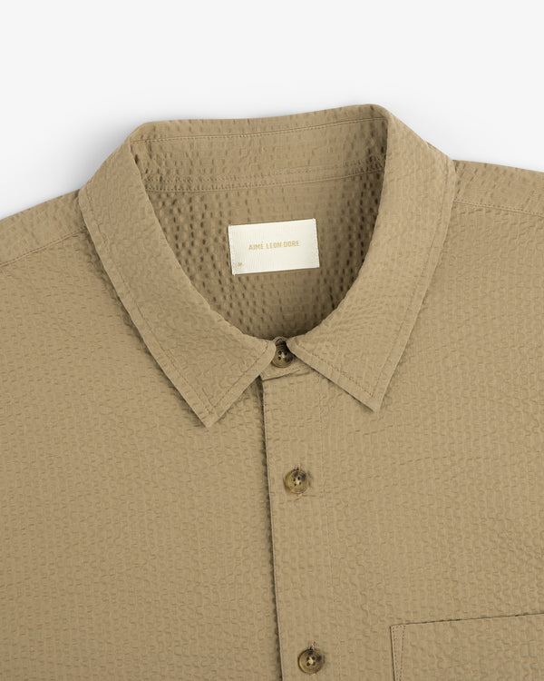 Close-up of a beige Short-Sleeve Seersucker Shirt with button-up front, collar, chest pocket, and visible inner label.