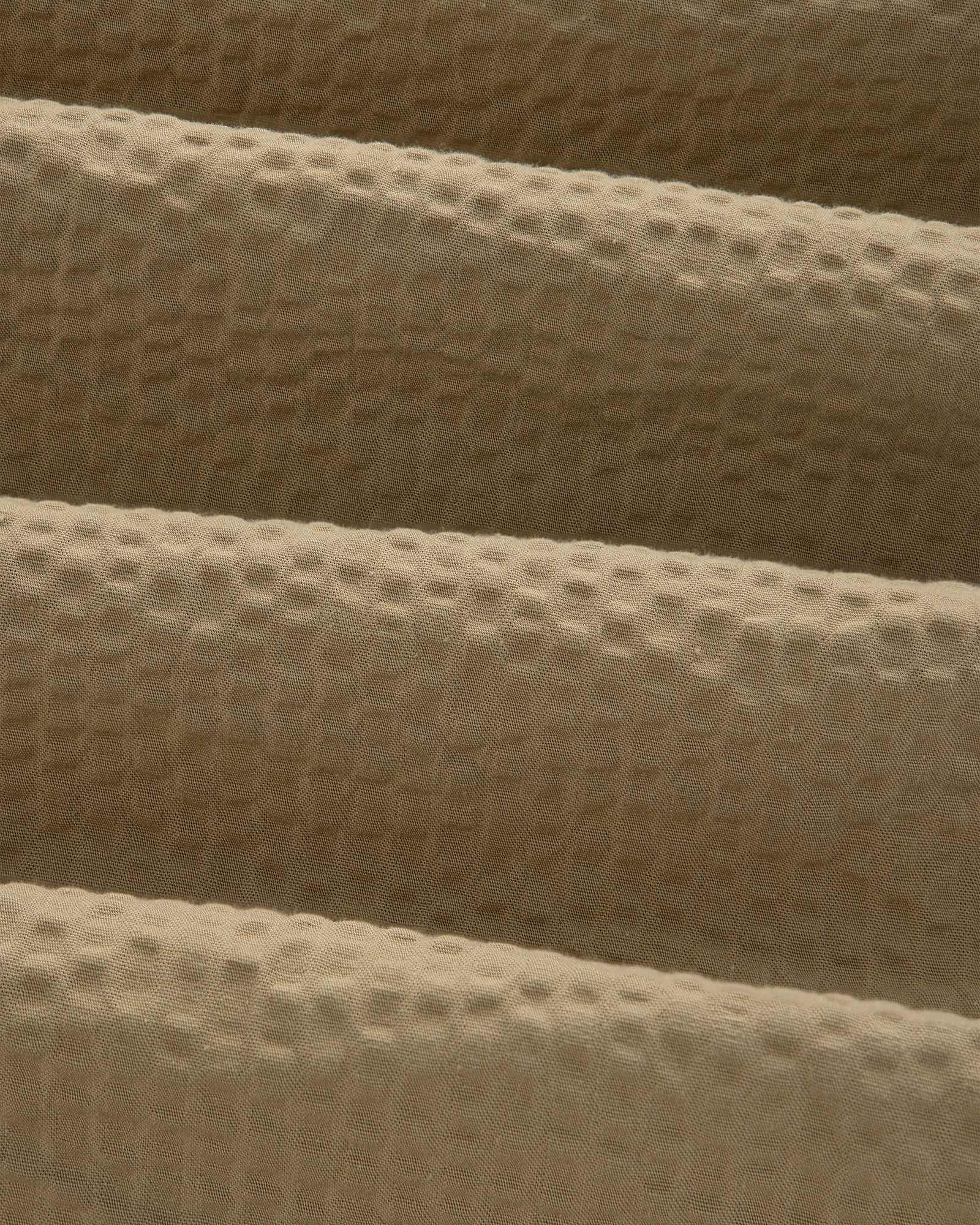Close-up of beige, waffle-textured fabric with gentle folds on a Short-Sleeve Seersucker Shirt.