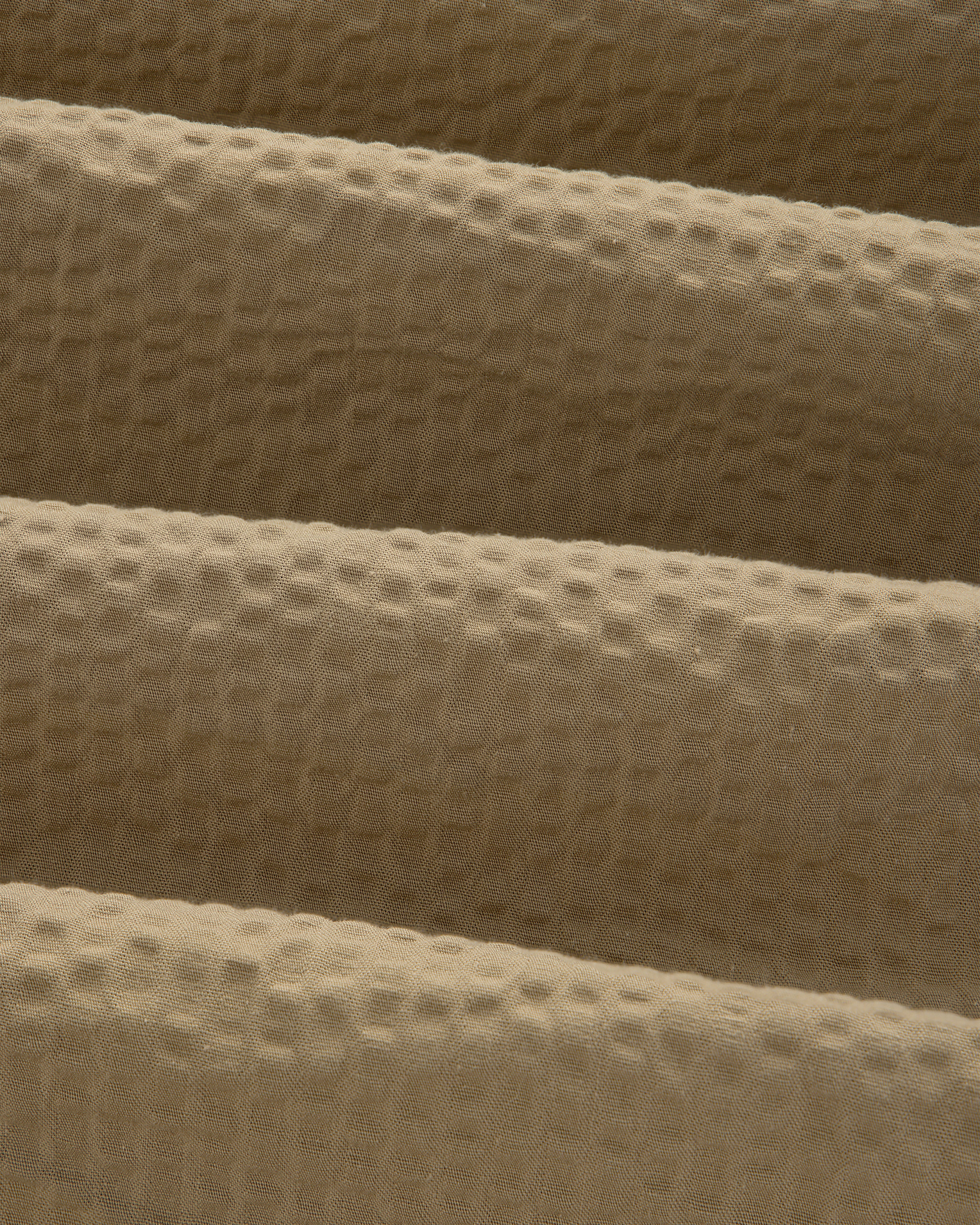 Close-up of beige, waffle-textured fabric with gentle folds on a Short-Sleeve Seersucker Shirt.