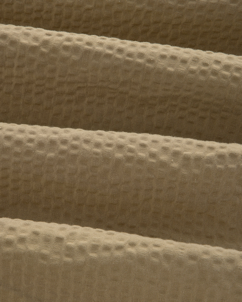 Close-up of beige, waffle-textured fabric with gentle folds on a Short-Sleeve Seersucker Shirt.