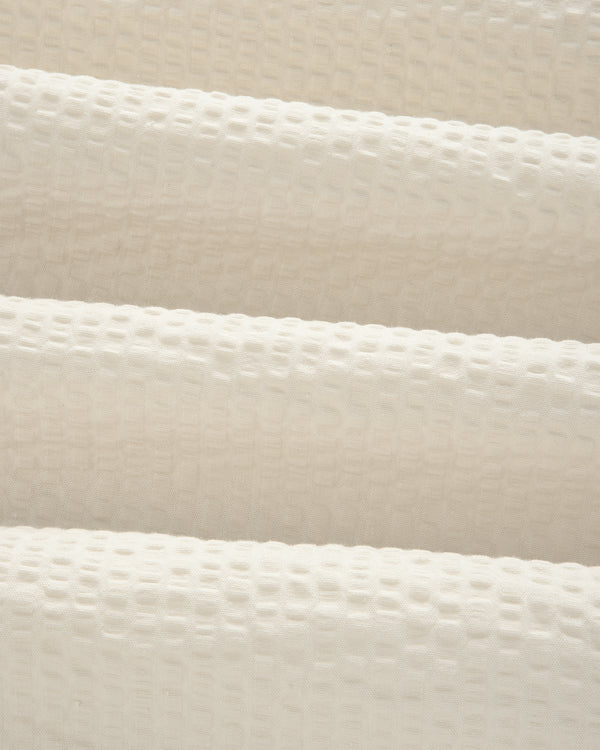 Close-up of the Short-Sleeve Seersucker Shirt's cream, textured fabric with a raised grid pattern and soft folds.