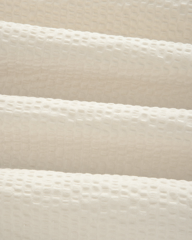 Close-up of the Short-Sleeve Seersucker Shirt's cream, textured fabric with a raised grid pattern and soft folds.