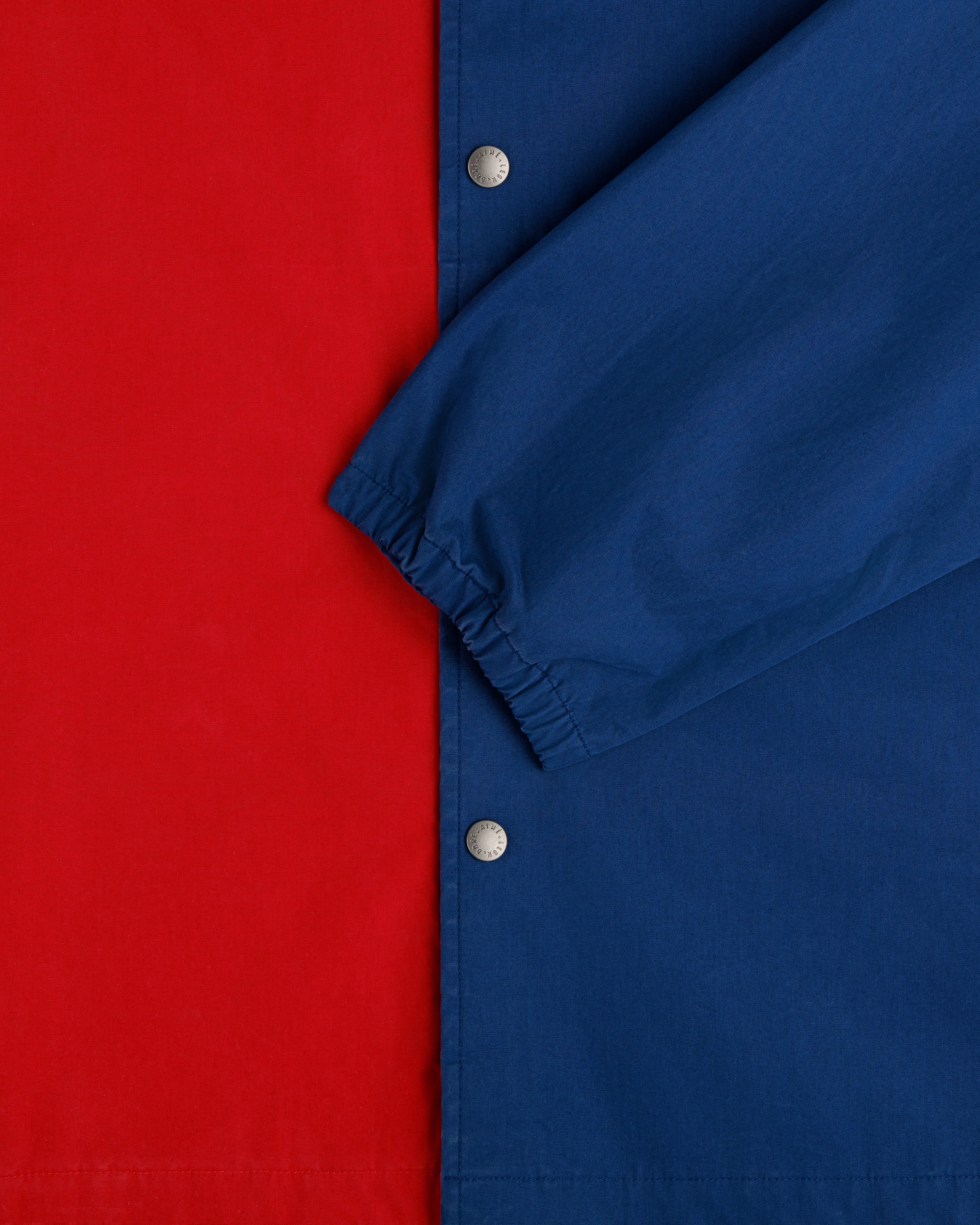 Close-up of the Marina Jacket with a red body, blue sleeve, silver snap buttons, and an elastic cuff.