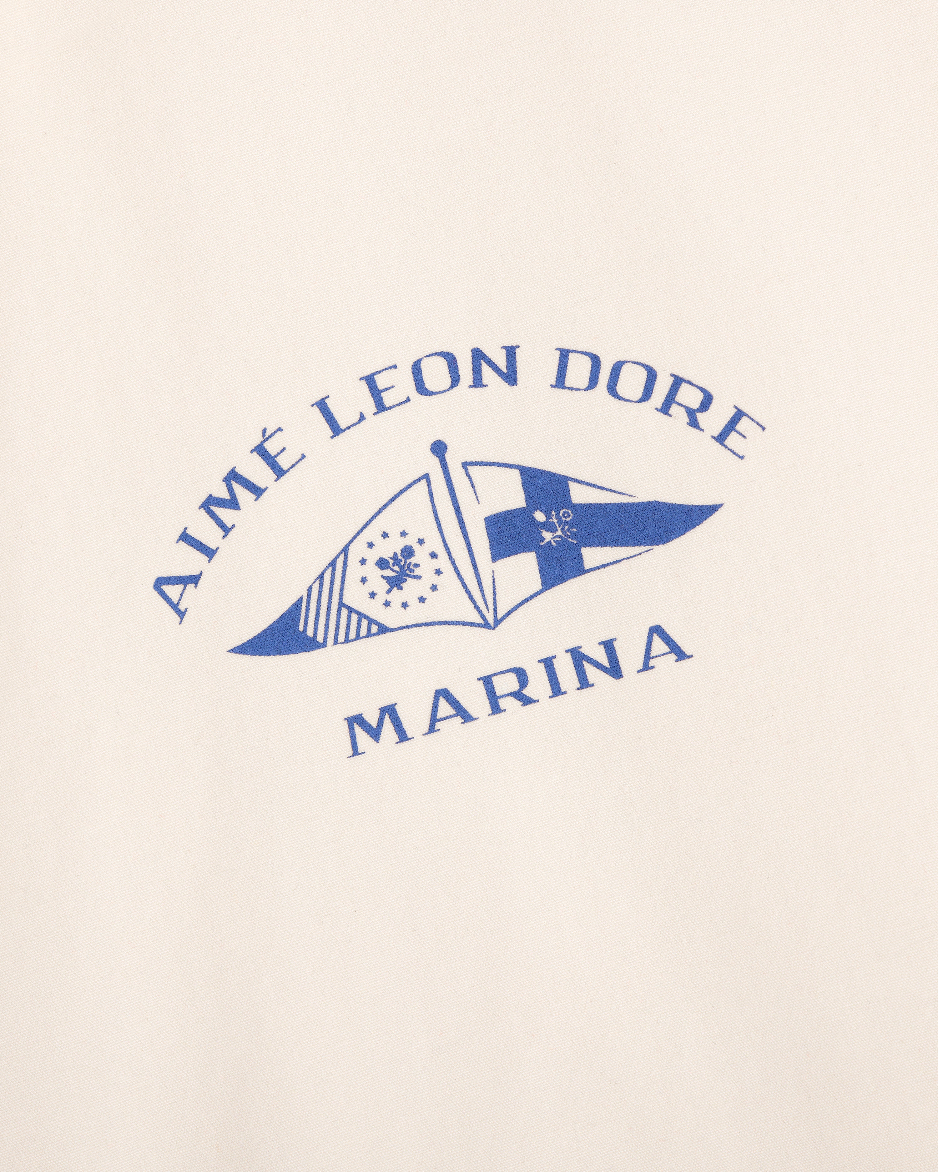 The Marina Jacket features a blue Aimé Leon Dore logo with two nautical flags on a cream background.