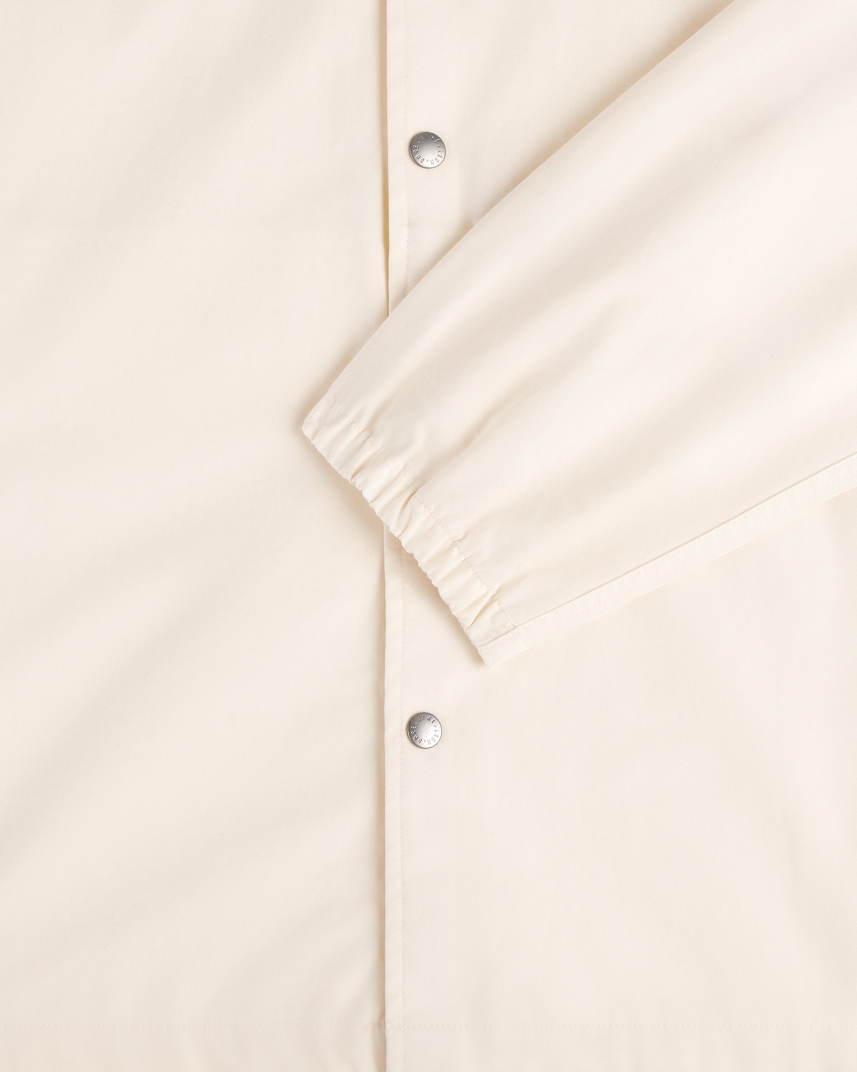Close-up of the Marina Jacket in cream with silver snap buttons and elasticated sleeve cuffs.